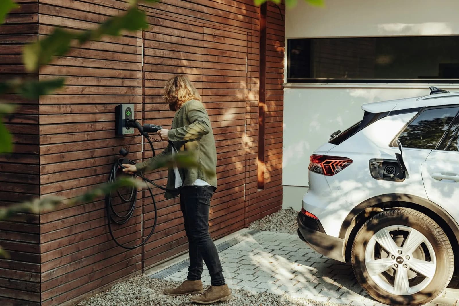 Un conducteur branche sa voiture électrique à la borne murale de sa maison